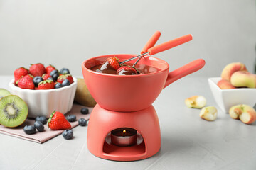 Fondue pot with chocolate and different products on grey table