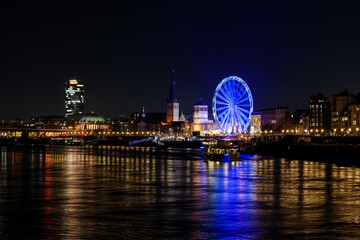 Night scenery on promenade and cityscape along riverside of Rhine river and background of Ferris wheel of Christmas market festival, Weihnachtsmarkt, in Düsseldorf, Germany.