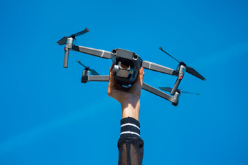 Woman holding drone or quadcopter isolated on the blue sky background. Flying drone outside in summer.