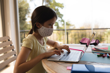 Girl wearing face mask using laptop at home