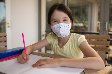 Portrait of girl wearing face mask doing homework at home