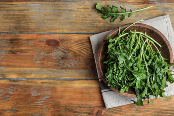 Fresh arugula in bowl on wooden table, flat lay. Space for text