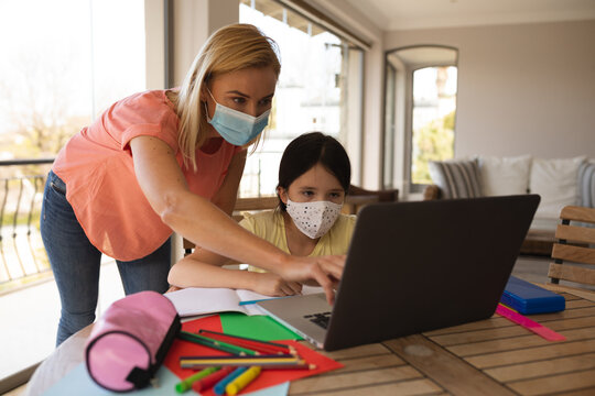 Mother and daughter wearing face masks using laptop at home