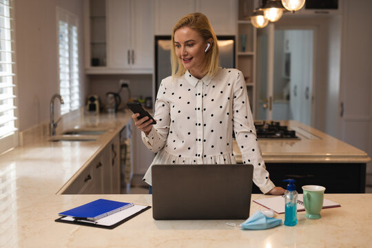 Woman wearing wireless earphones talking om smartphone in the kitchen