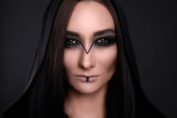 Naklejka premium Mysterious witch in mantle with hood on black background, closeup