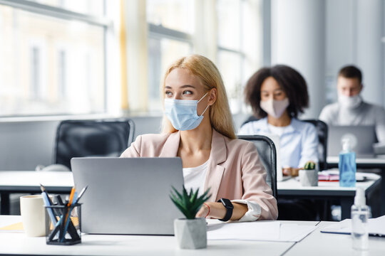 Modern coworking office worker after returning from covid quarantine to office. Millennial woman in protective mask with smart watch looks at window