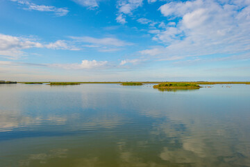 The edge of a lake in a green grassy field in sunlight under a blue cloudy sky in autumn, Almere, Flevoland, The Netherlands, September 29, 2020