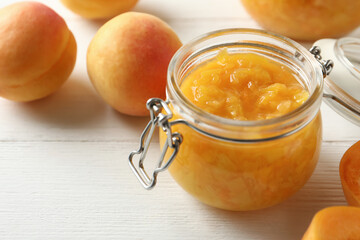 Jar of apricot jam and fresh fruits on white wooden table, closeup