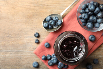 Jar of blueberry jam and fresh berries on wooden table, top view. Space for text