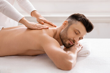 Side view of relaxed man having body massage at spa