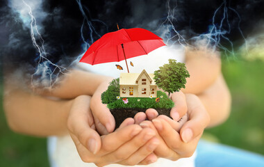 Insurance concept - umbrella demonstrating protection. Family holding house model with green lawn,...