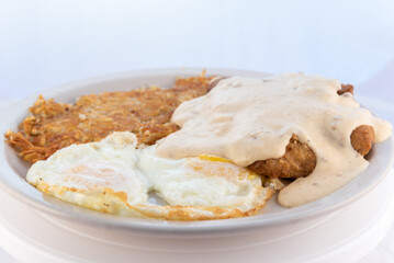 Generous serving meal of a hearty chicken fried steak, eggs, and hash browns dripping with country...