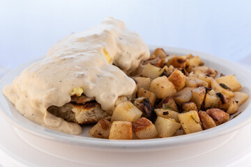 Generous serving meal of a hearty biscuit, eggs, potatoes covered in country gravy