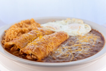 Generous serving meal of a hearty pair of breakfast enchiladas combined with refried beans, rice, and eggs