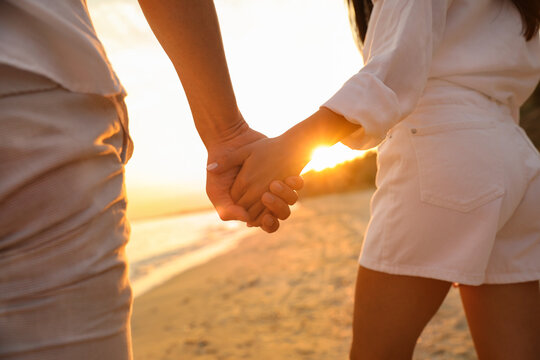 Lovely couple holding hands on beach at sunset, closeup