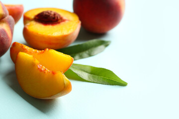 Slices of fresh ripe peach and green leaves on light blue background, closeup. Space for text