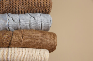 Stack of folded knitted sweaters on beige background, closeup. Space for text