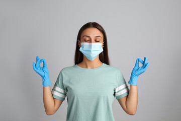 Woman in protective mask meditating on grey background. Dealing with stress caused by COVID‑19 pandemic