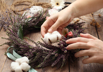 Florist making beautiful autumnal wreath with heather flowers at wooden table, closeup