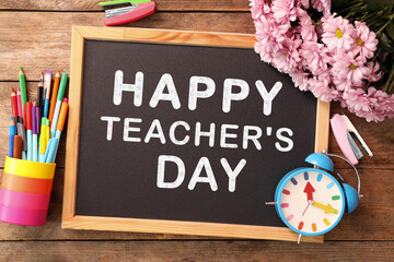 Small blackboard with text Happy Teacher's Day, stationery and flowers on wooden table, top view