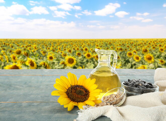Sunflower oil and seeds on blue wooden table near blooming field. Space for text