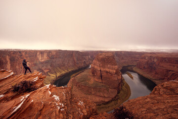 Man taking a photo on horseshoe bend on Colorado River at dawn in cloudy weather. Panoramic view of horseshoe bend