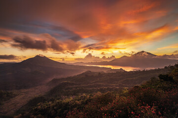 Obraz premium Beautiful mountain landscape during sunrise. Hills, Batur volcano and lake. Scenic panoramic view. Colorful sky with clouds. Foggy morning. Kintamani, Bali
