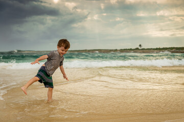 Toddler playing at the beach during a hot cloudy day, with waves coming in  from the emerald color...