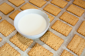 a cup full of milk and cookies laid out in a diagonal pattern on an abstract light wooden background