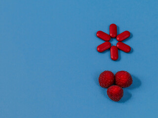 red pills with raspberries
Six red pills and three fresh raspberries lie hardly on a blue background on the right with space for text on the left, close-up top view.