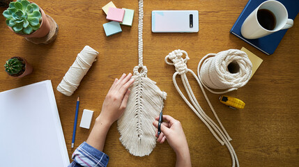 A young woman working on custom macrame decor with tools over a creative desktop