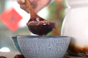Close-up shot of Laba porridge filled into a bowl with a wooden spoon
