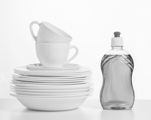 Black and white image of a gel bottle and a set of dishes on a white table.