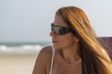 Retrato de mulher usando óculos de sol, com cabelos longos na praia em dia ensolarado 