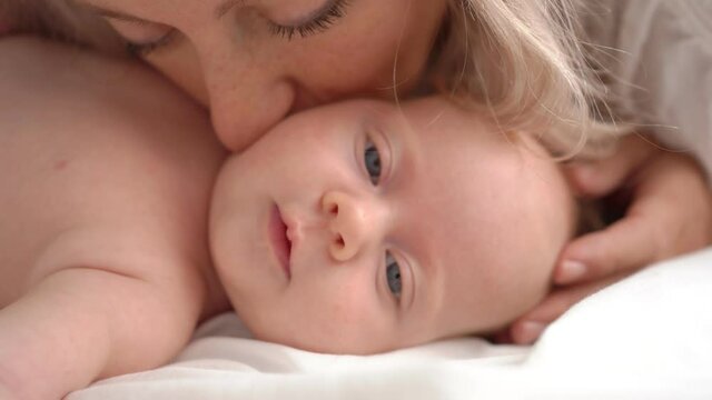 mother kisses the baby lying in bed. concept of maternal love, newborn care.