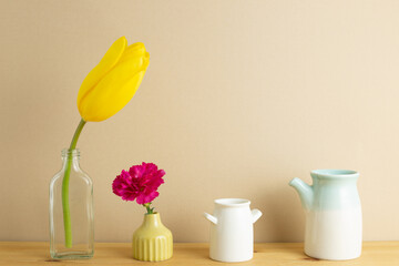 Yellow tulip and pink carnation flower in vase on wooden table with beige background. floral arrangement, copy space