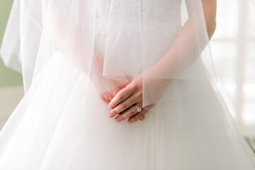 Close-up of a bride holding her hands over her wedding dress. She is wearing a veil. 