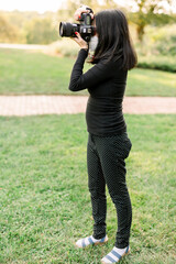 Asian photographer wearing all black taking photographs outside in a grassy area. 