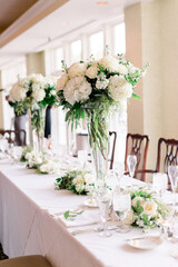 A pretty table decorated with two tall vases with a white and green flower arrangement centerpiece. 