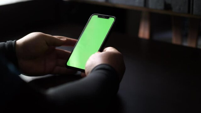 Close up and slide movement of a man facetime with a smartphone. Chroma key green screen on the smartphone screen. A man scrolls information on the phone screen.