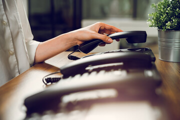 close up hand holding black landline on the table in office.