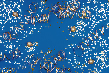 Fototapeta na wymiar Holiday background with confetti, balls and ribbons on classic blue. Seasonal Christmas celebration backdrop