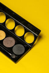Close-up of eyeshadow palettes with brushes isolated on yellow background. Beauty industry and make-up products.