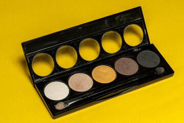 Close-up of eyeshadow palettes with brushes isolated on yellow background. Beauty industry and make-up products.
