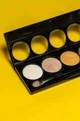 Close-up of eyeshadow palettes with brushes isolated on yellow background. Beauty industry and make-up products.
