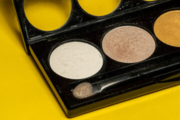 Close-up of eyeshadow palettes with brushes isolated on yellow background. Beauty industry and make-up products.