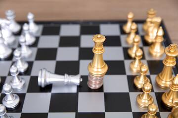 The silver queen pawn on the chess board kneels to the golden queen pawn standing on the coin