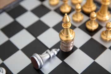 A silver chess piece on a chess board kneels down to a golden chess piece standing on a coin