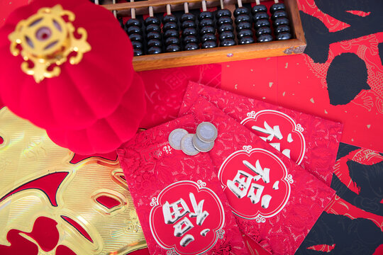 Red envelopes and traditional abacus and red lanterns and coins on red spring couplets background. The Chinese character on the red envelopes and spring couplets mean "happiness"