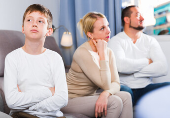 Upset son and frustrated parents sitting on sofa and looking away after quarrel